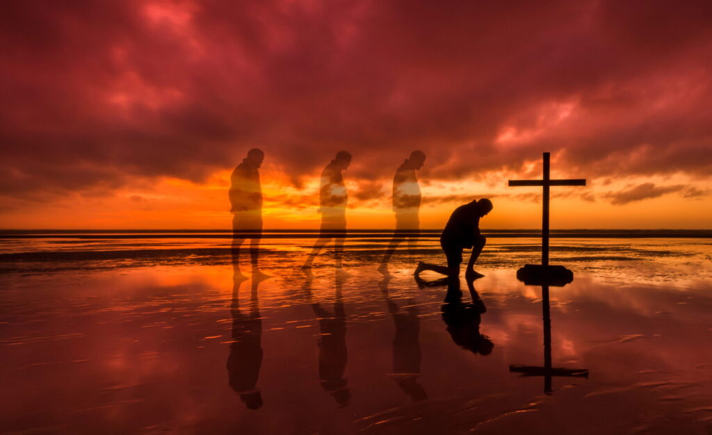 the outline of a man walking up and kneeling before a cross on the beach at sunset with the waves and the sunset in the background