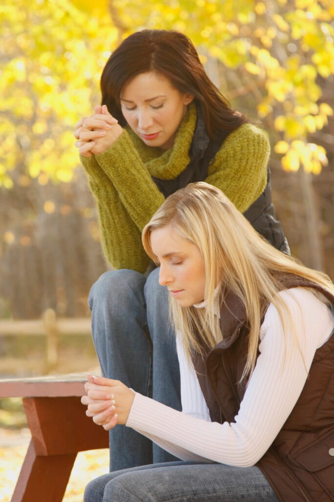 women praying together outside at park bench